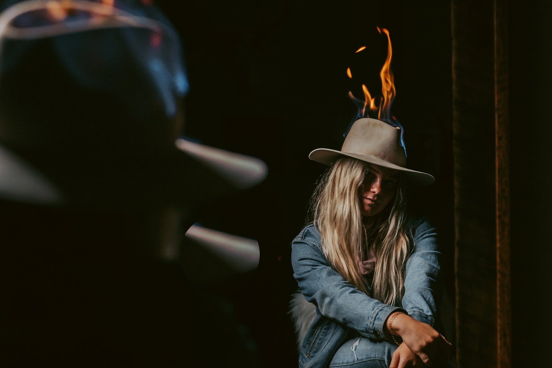 Person sitting by a fire wearing a hat with flames on it