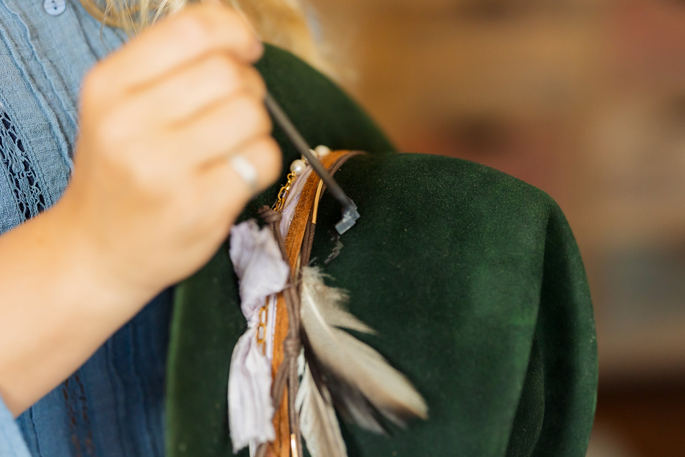 Person holding a felt hat fabric with feathers and ribbons, blurred background