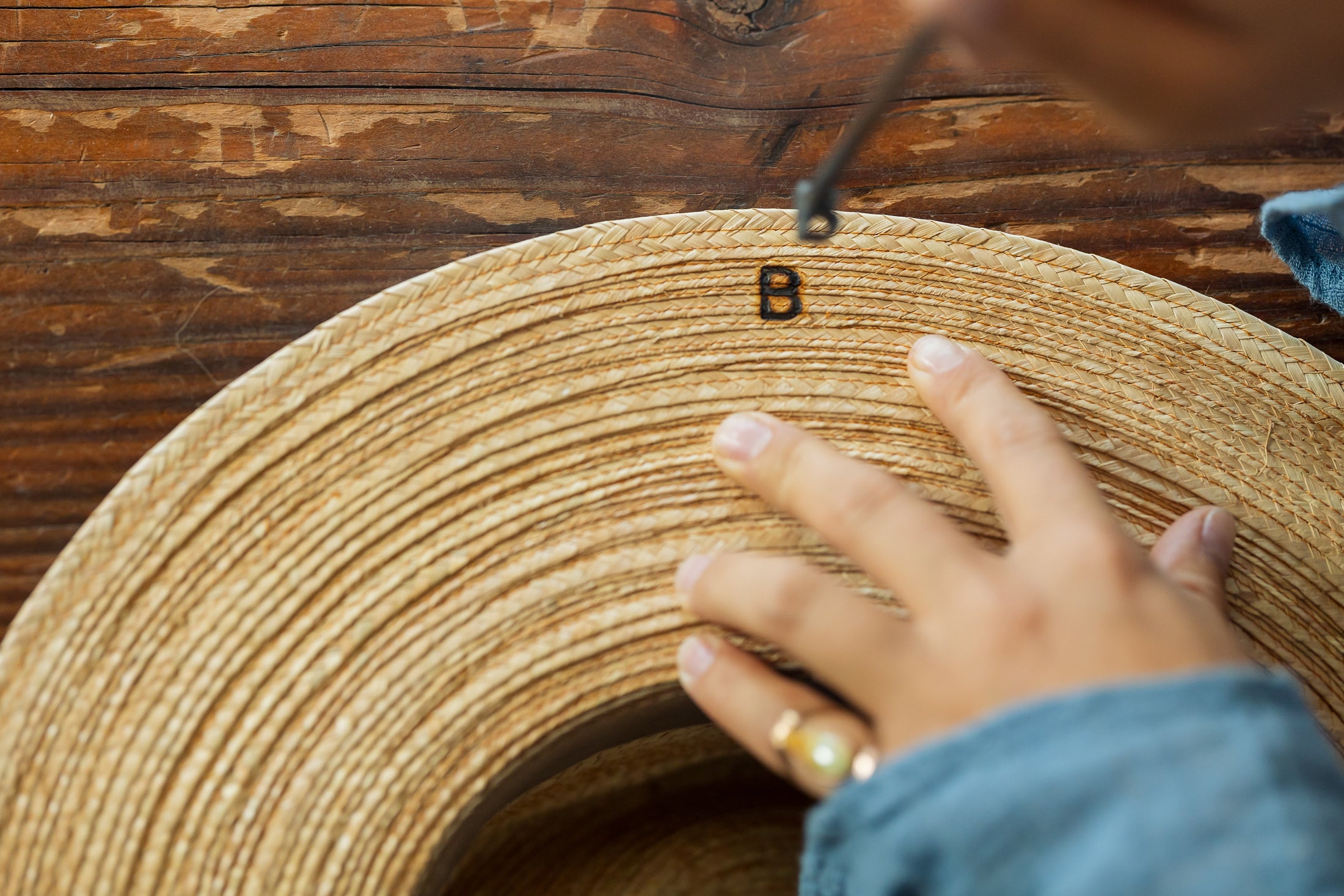 Hand branding a woven hat against a wooden background