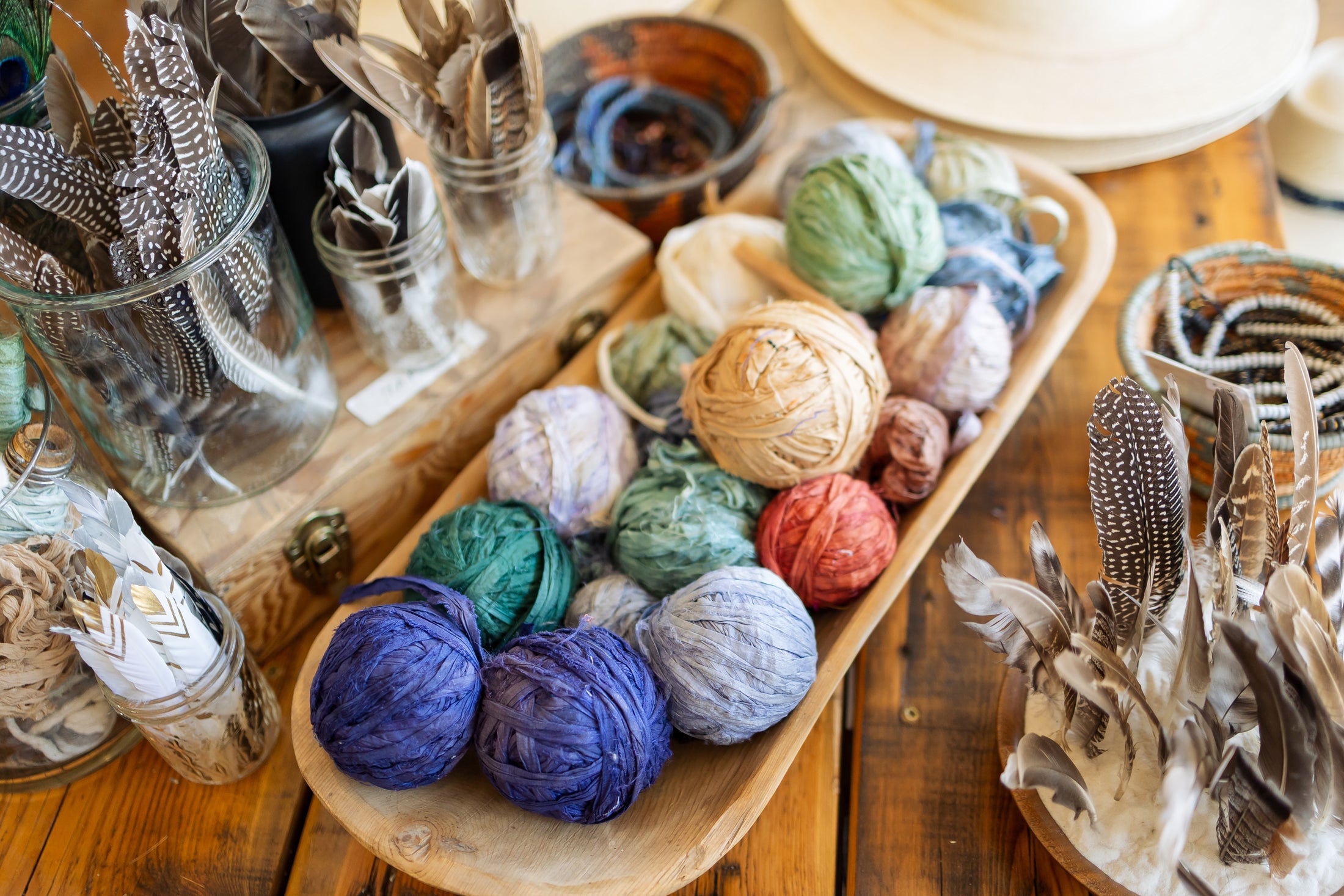 Colorful yarn balls in a wooden bowl on a wooden surface with various craft materials.