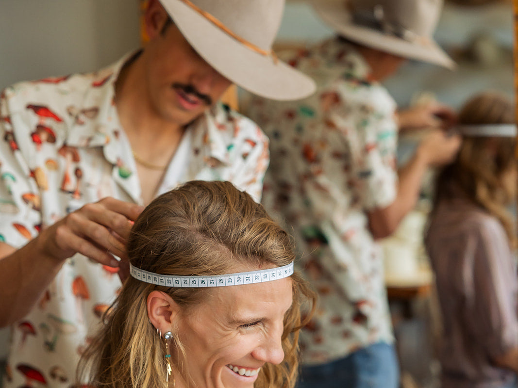 Person getting their head measured by another person in a casual setting for a western hat.