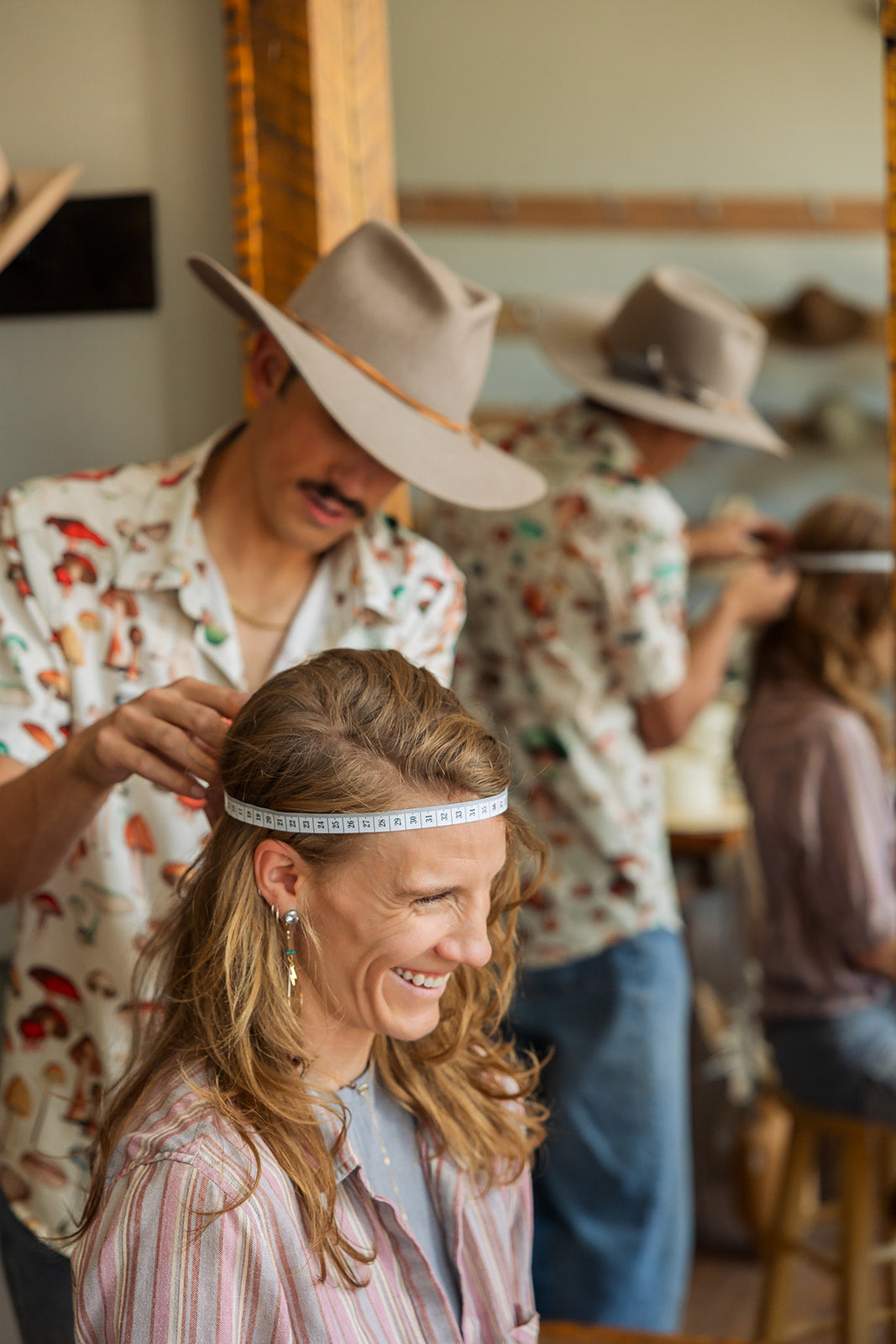 Person getting their head measured by another person in a casual setting for a western hat.