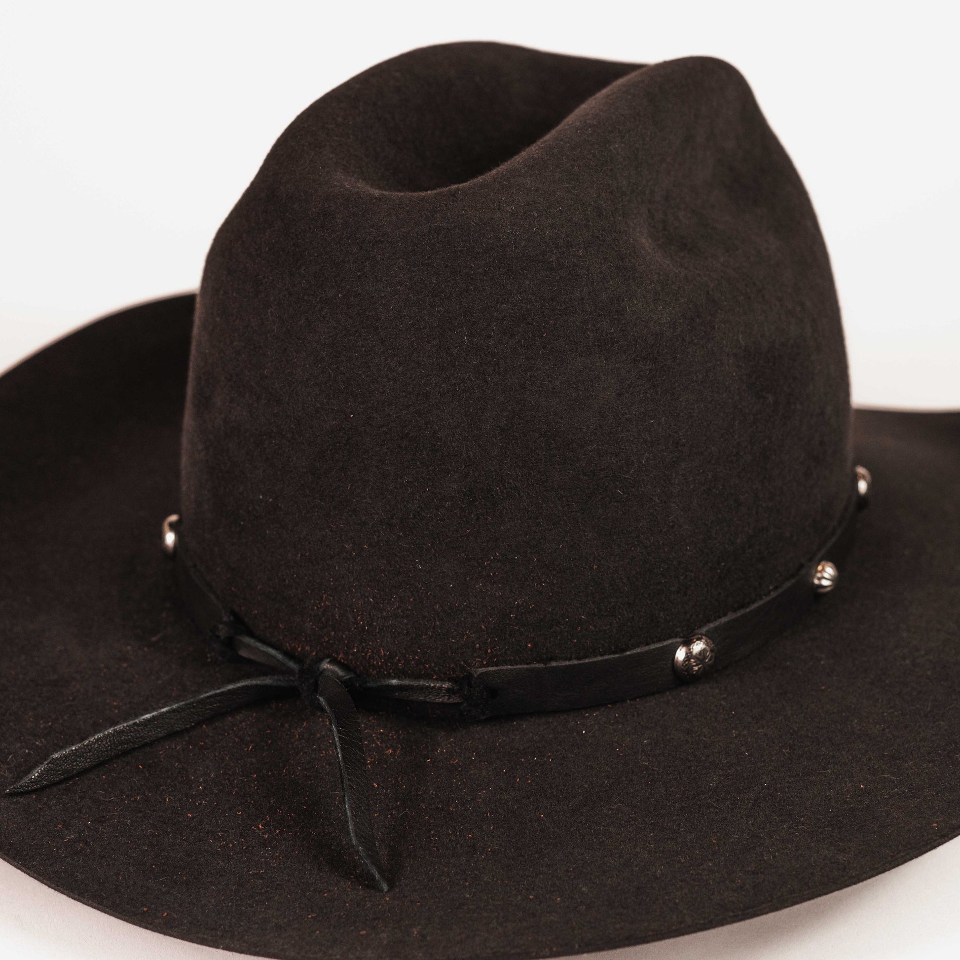 A black felt wide-brimmed cowboy hat with a black ribbon band and small silver studs, photographed on a plain white background.