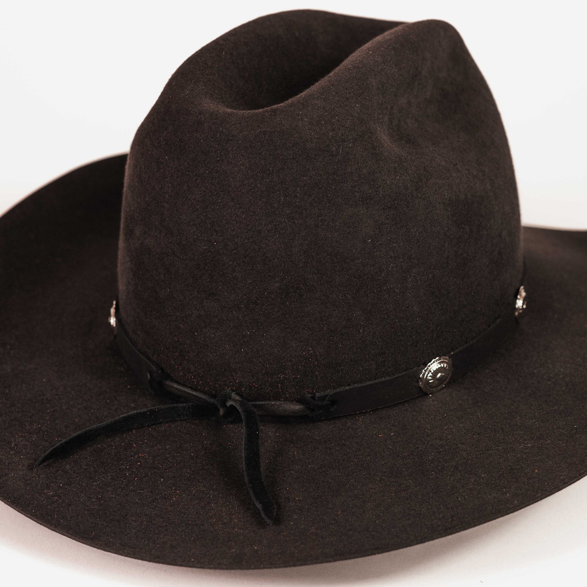 A dark brown felt cowboy hat with a black ribbon band and silver conchos, photographed on a clean white background.