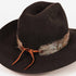 A black felt cowboy hat with a brown leather tie and a feathered band in brown, gray, and blue tones, shown on a plain white background.