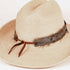 A light beige woven straw hat with a brown leather ribbon band tied in a bow, decorated with dark brown feathers and a small metallic concho accent.