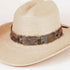 A light beige woven straw fedora hat with a dark brown feather band around the crown, photographed on a clean white background.