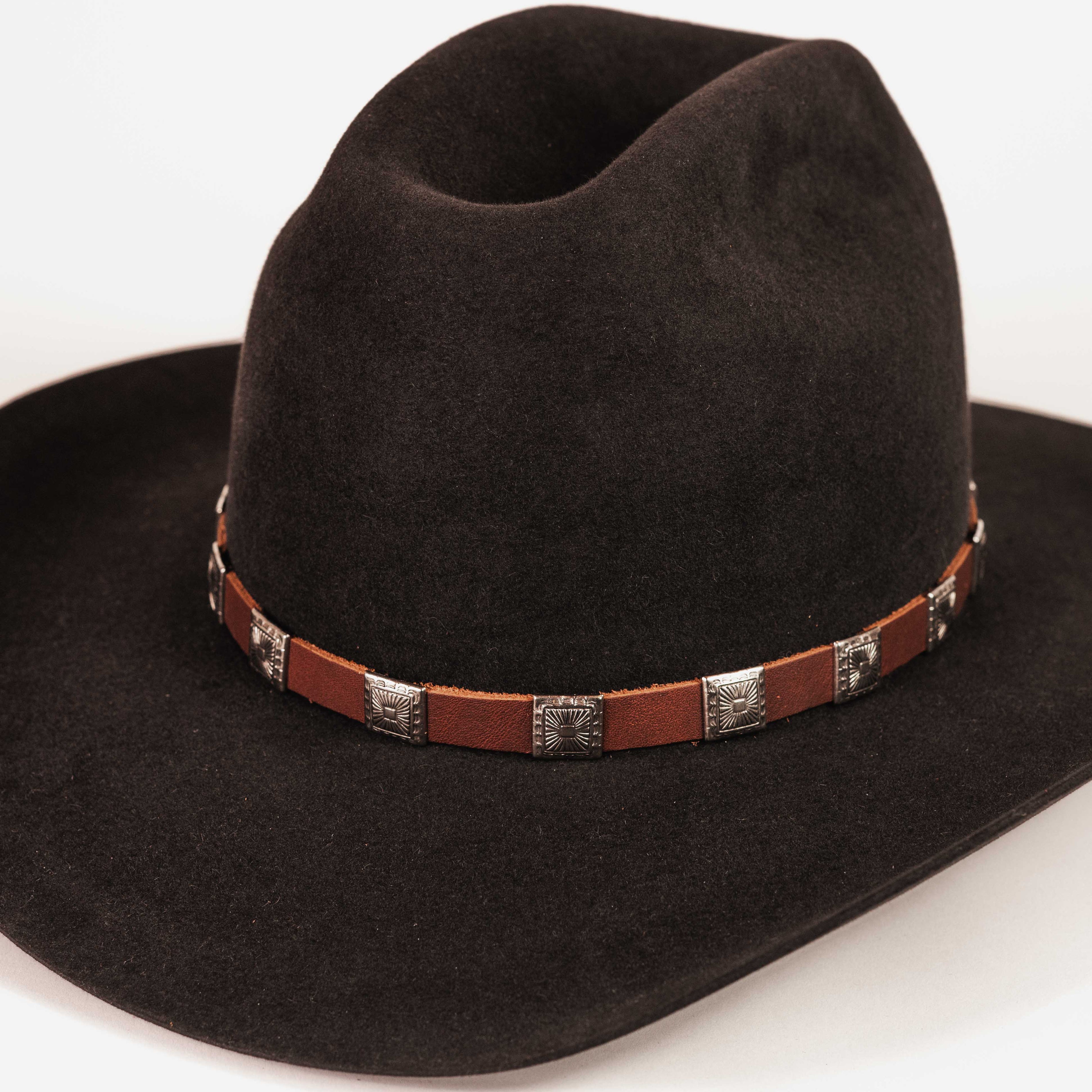 A black felt cowboy hat with a brown leather band decorated with silver-toned metal conchos, shown on a plain white background.