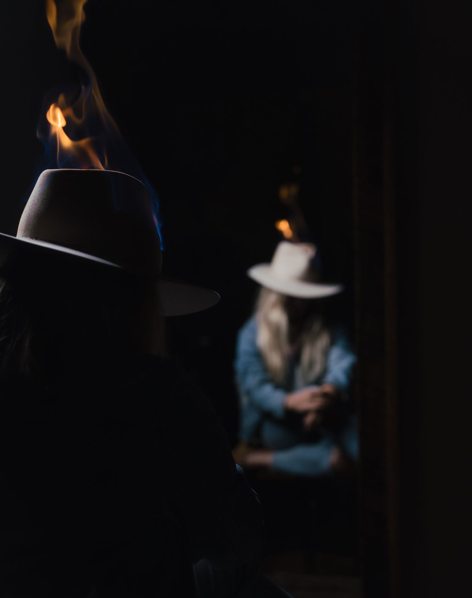 Person wearing a hat with fire coming out of it, standing in front of a mirror.