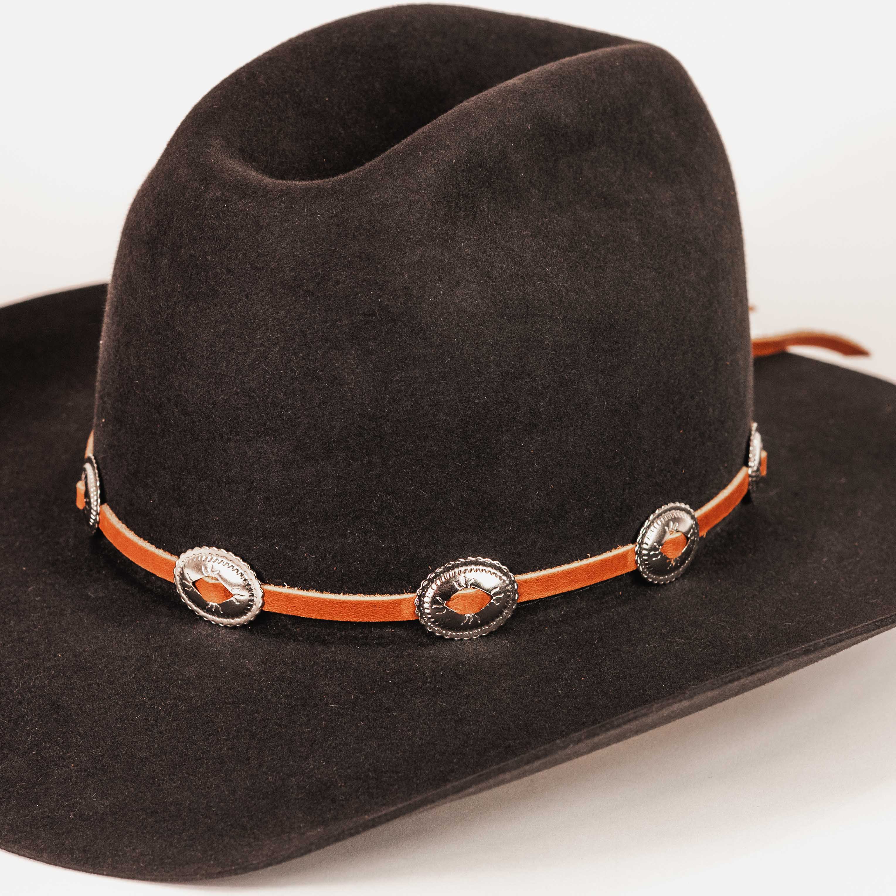 A dark brown felt cowboy hat with a vibrant orange leather band decorated with silver-toned conchos and orange inlays, shown on a clean white background.