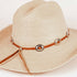 A light beige woven straw cowboy hat with a brown leather band decorated with silver-tone conchos and orange accents, shown on a plain white background.