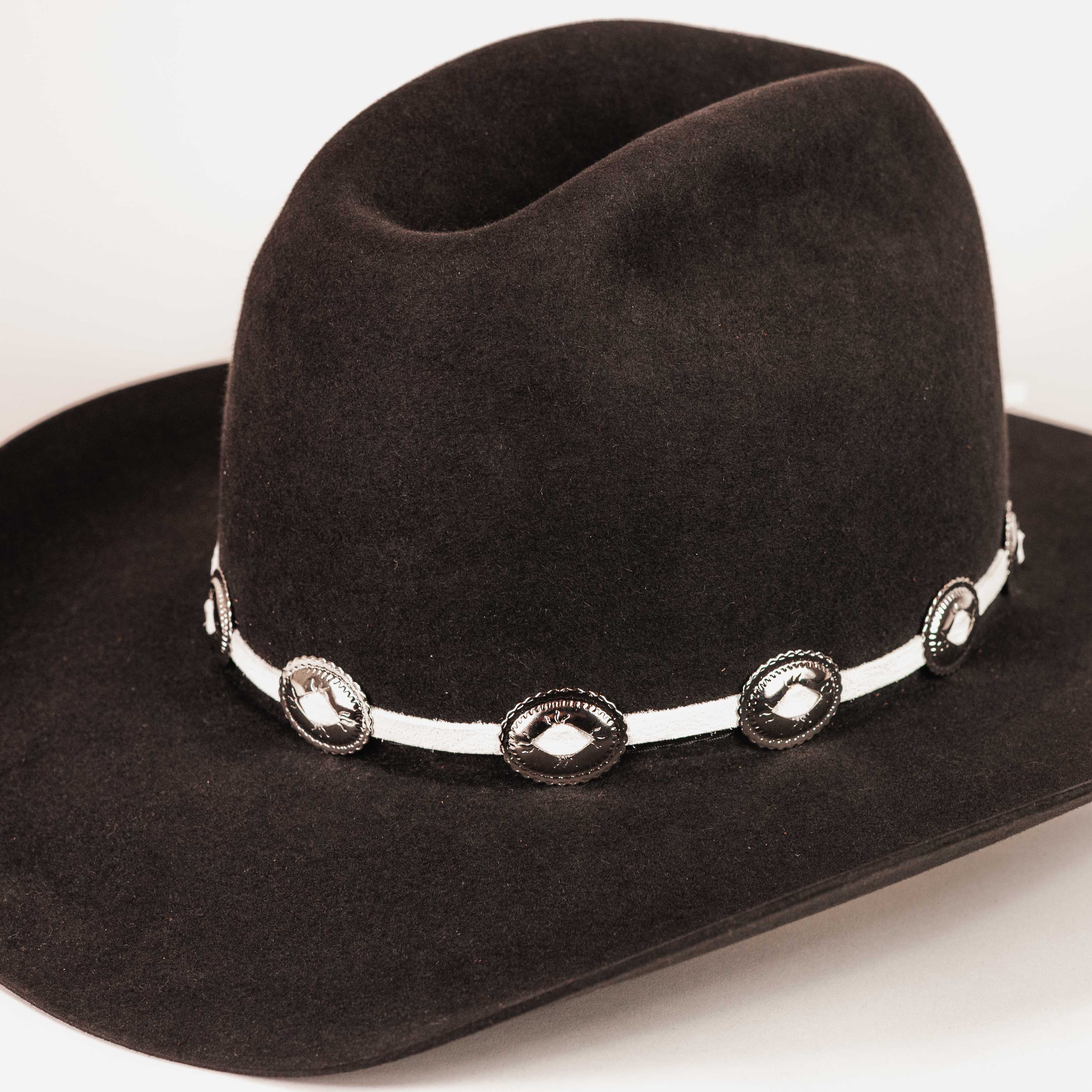 A black felt cowboy hat with a white band decorated with silver conchos, shown on a plain light background.