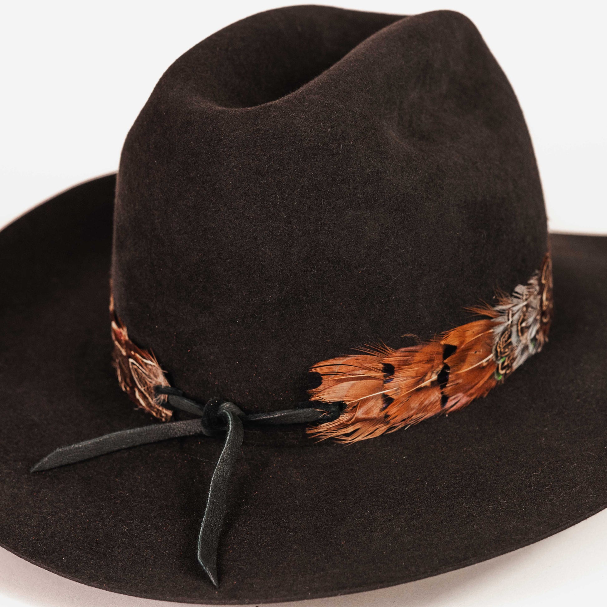 A black felt cowboy hat with a decorative band featuring brown feathers and a black ribbon tie, shown against a plain white background.