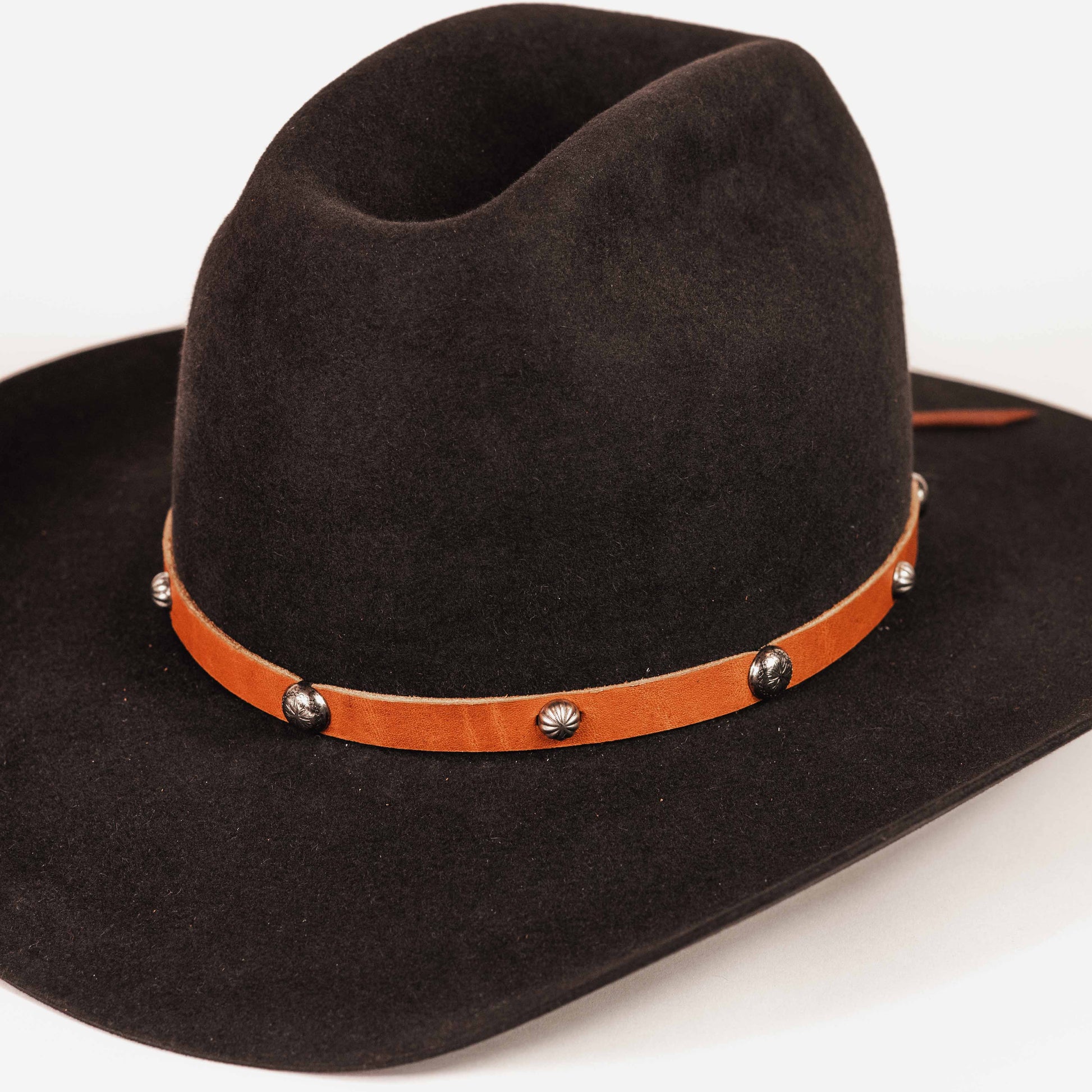 A black felt cowboy hat with a brown leather band decorated with silver conchos, shown on a plain white background.