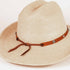 A light beige woven straw fedora hat with a brown leather band decorated with silver-tone studs and a bow, shown on a plain white background.