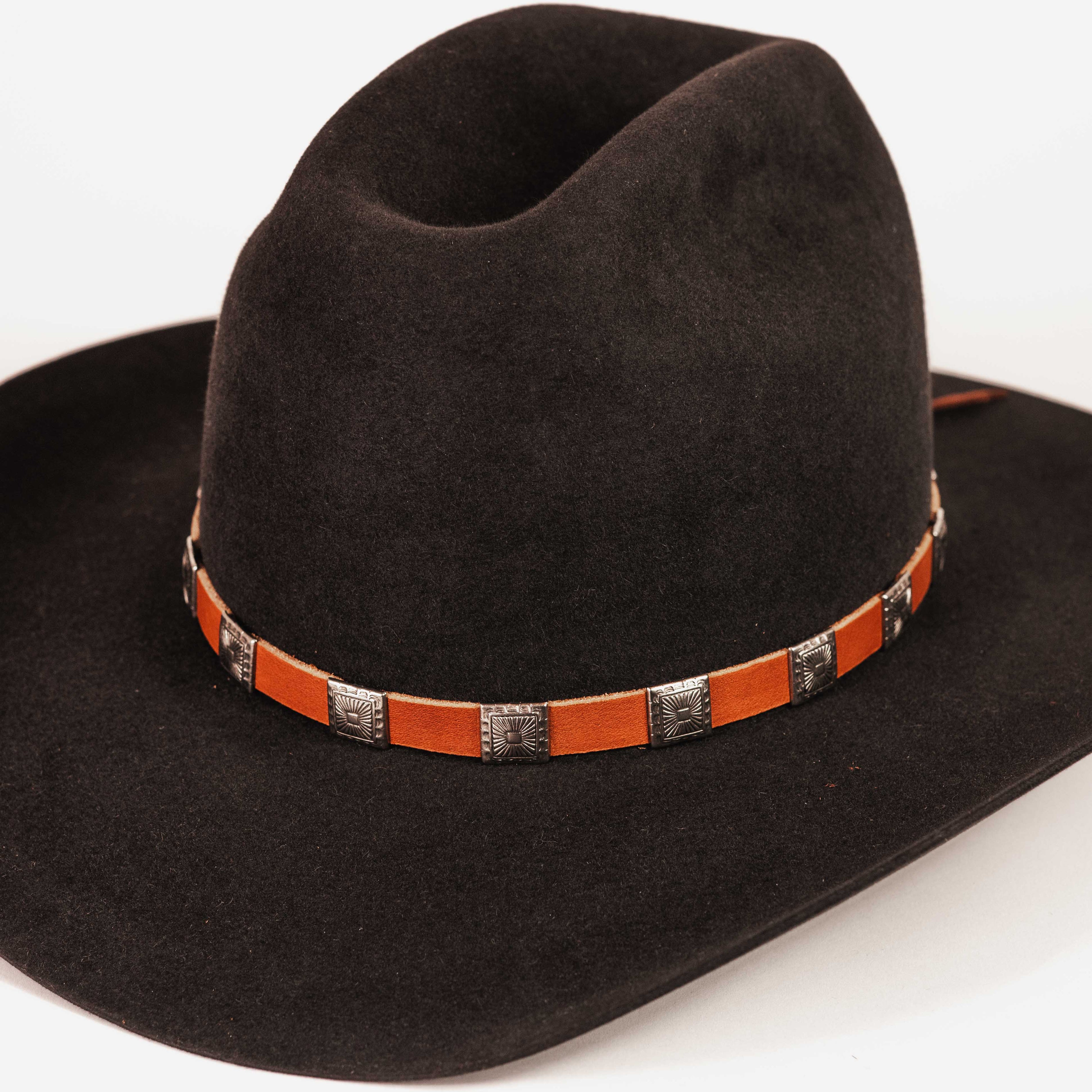 A black felt cowboy hat with a brown leather band decorated with silver conchos, shown on a plain white background.